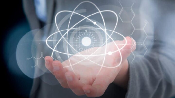 Montagem com pessoa segurando ilustração grande de átomo