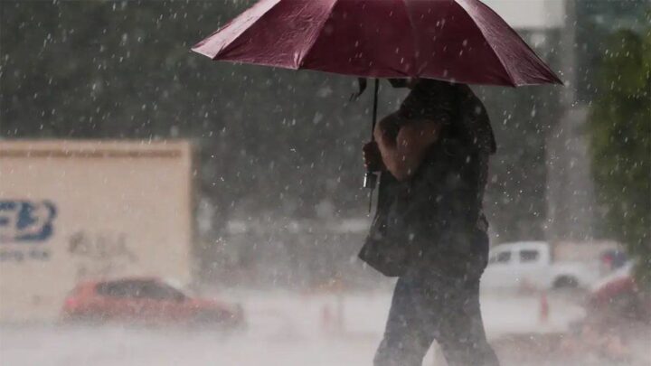 Mulher andando na rua com guarda-chuva aberto durante chuva