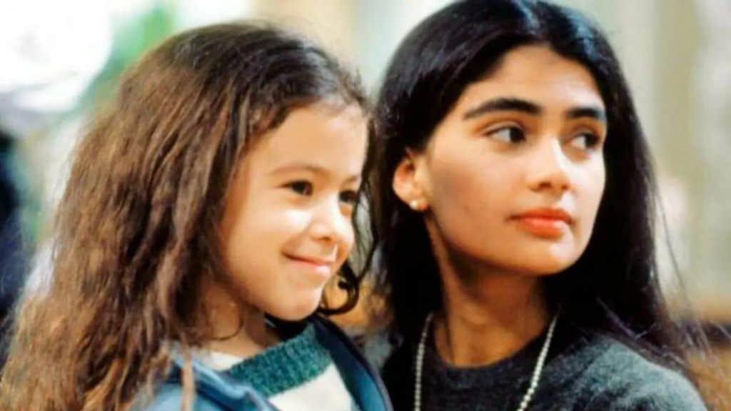 Duas personagens femininas estão lado a lado. Uma menina de cabelos longos e castanhos sorri, enquanto uma jovem mulher, com cabelos pretos lisos e expressão serena, olha para o lado