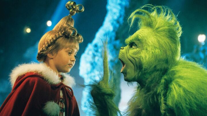 Cena do filme O Grinch. Um ser verde e peludo, o Grinch, aparece com expressão zangada, de boca aberta, enquanto interage com uma menina loira de cabelo elaborado e vestida com um casaco vermelho de Natal