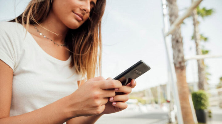 Mulher sentada em ambiente externo mexe no celular
