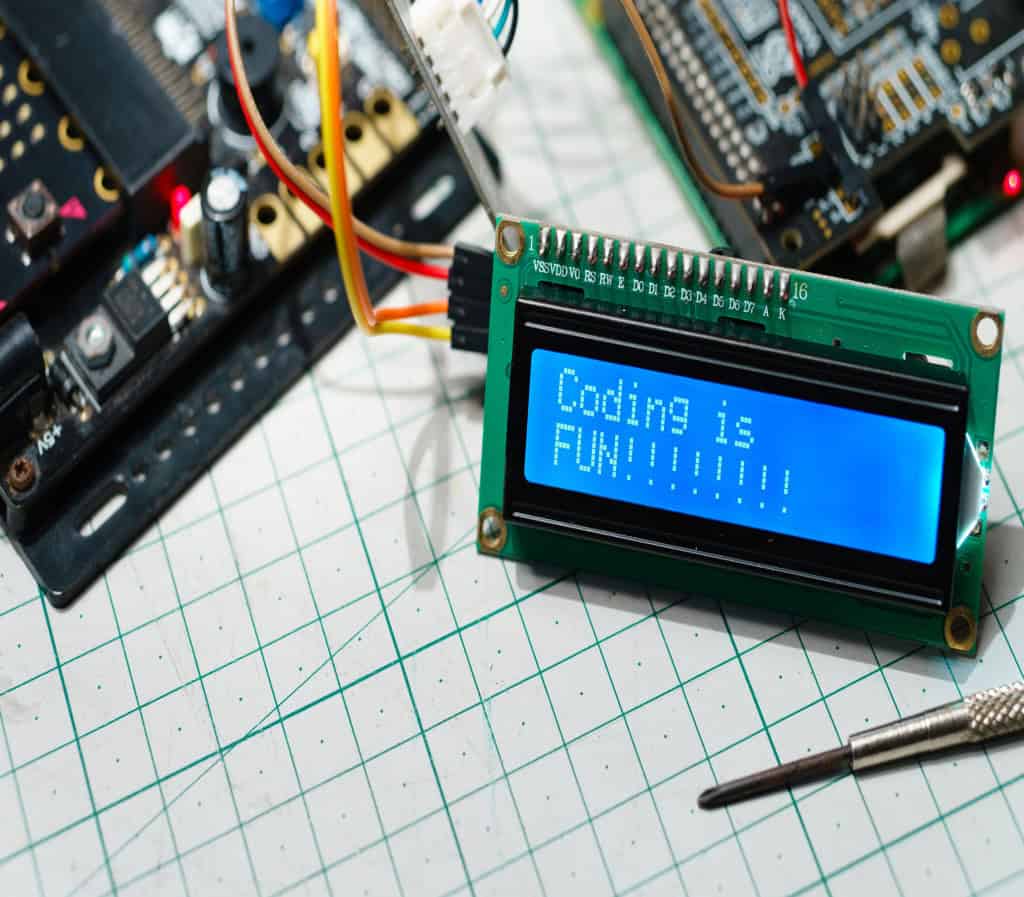 Detalhe, tela LCD azul exibindo a palavra "Programar é divertido!", fio conectado à placa e ao circuito do computador. Educação STEM, aprendizagem online e conceito de projeto de eletrônica.