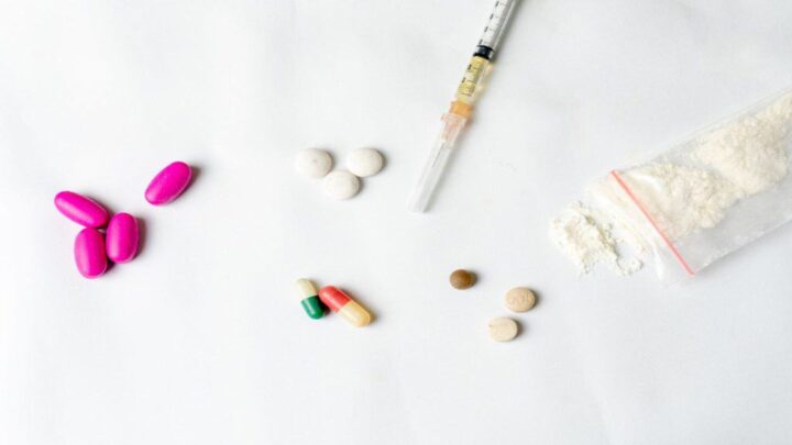 Substâncias narcóticas, pó de droga, seringa e pílulas brancas, pílulas rosas sobre um fundo texturizado branco. Conceito de vício e maus hábitos.