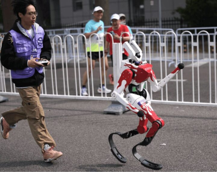 Integrante de uma equipe correndo atrás de um robô operado por controle remoto. 
