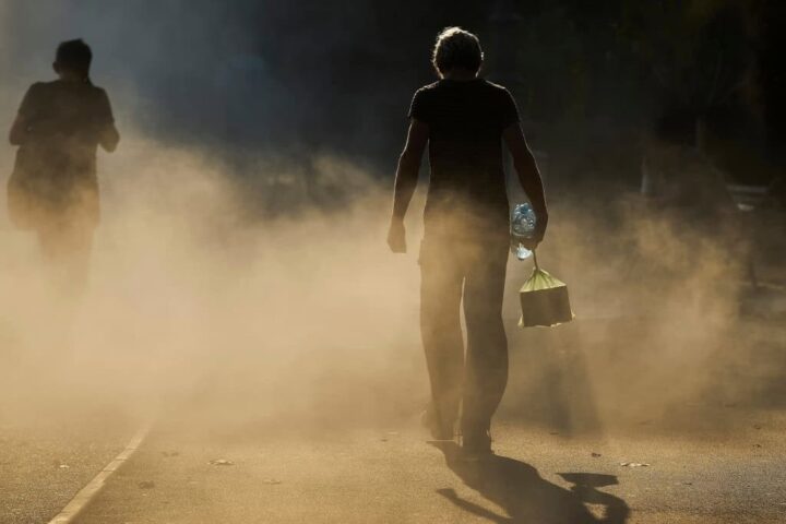 Pessoas caminham sob forte calor e poeira em uma rua